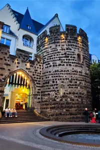 Sterntor- Mai 2025, The medieval Sterntor city gate in Bonn at dusk, with an illuminated archway, round tower, outdoor seating, and a fountain in the foreground.
